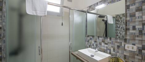 Une salle de bain moderne avec une douche à l’italienne en verre, un lavabo blanc et un mur recouvert de carreaux.