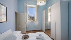 A bedroom with a bed, a bedside table, a window with curtains, and a mirror.