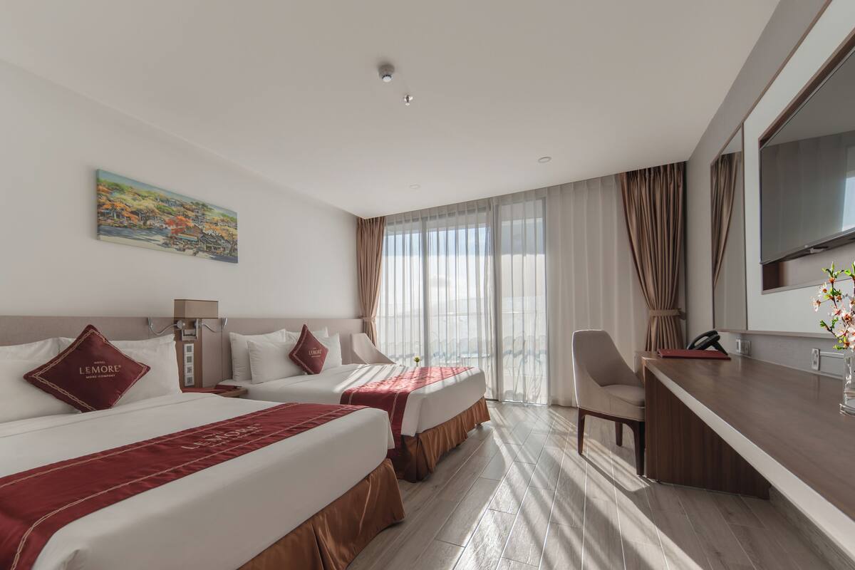 A hotel room with two beds, a desk, and a large window with curtains.