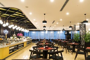 Restaurante com várias mesas e cadeiras, um balcão de buffet e luminárias pendentes.