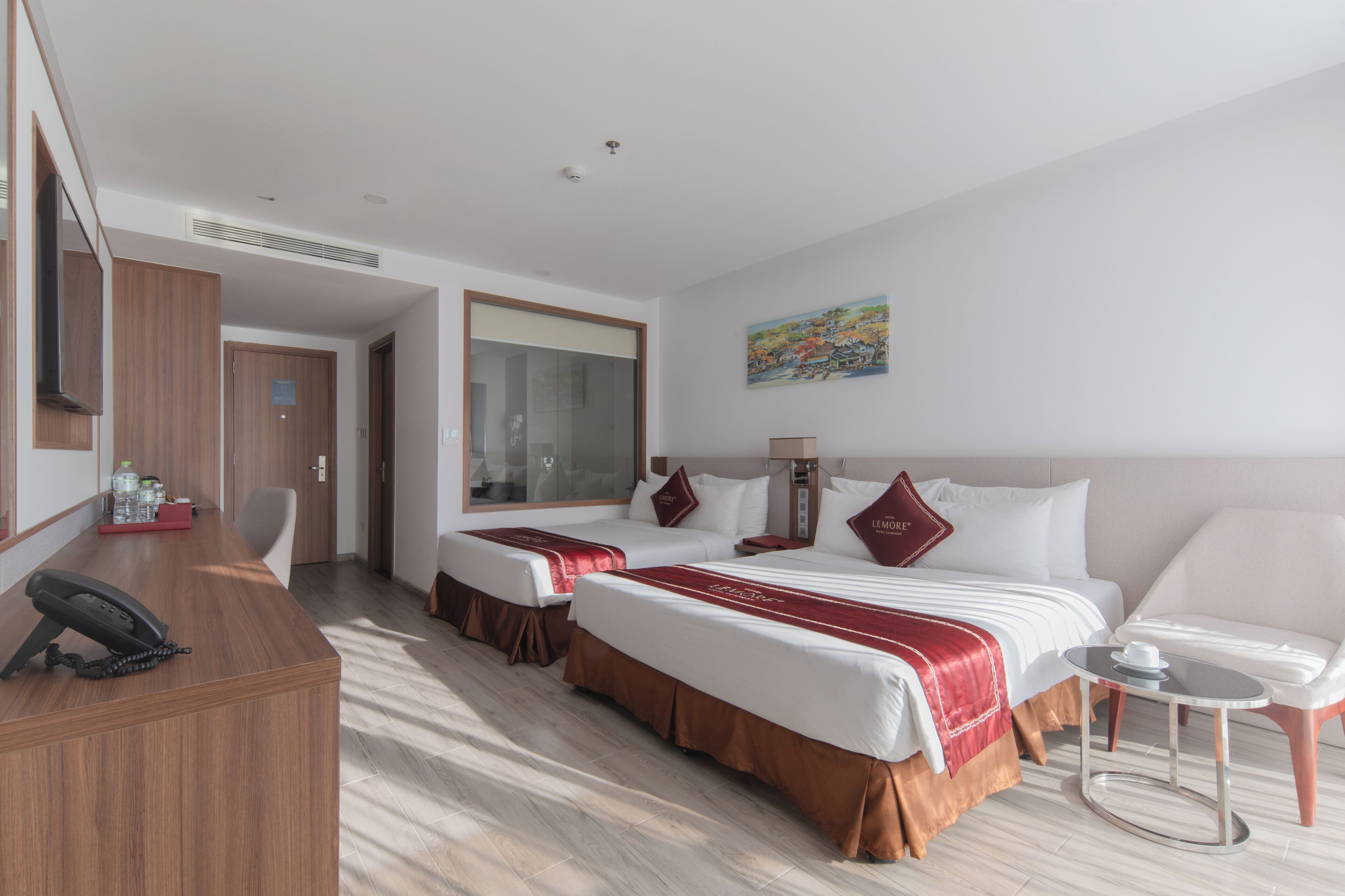 A hotel room with two beds, a desk with a telephone, a small table, and a painting on the wall.