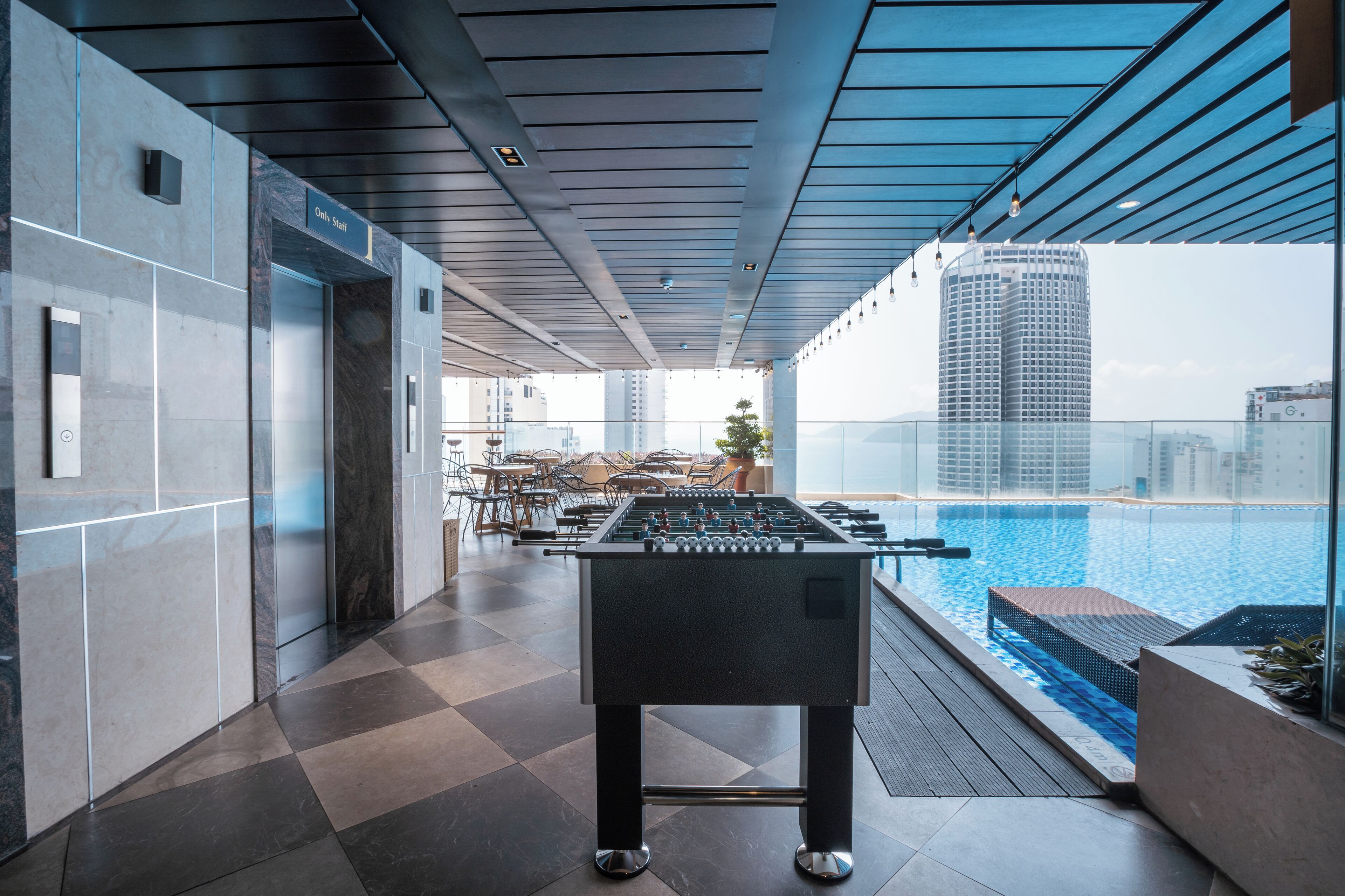 A modern indoor pool area with a foosball table, a glass-enclosed pool, and a view of high-rise buildings.