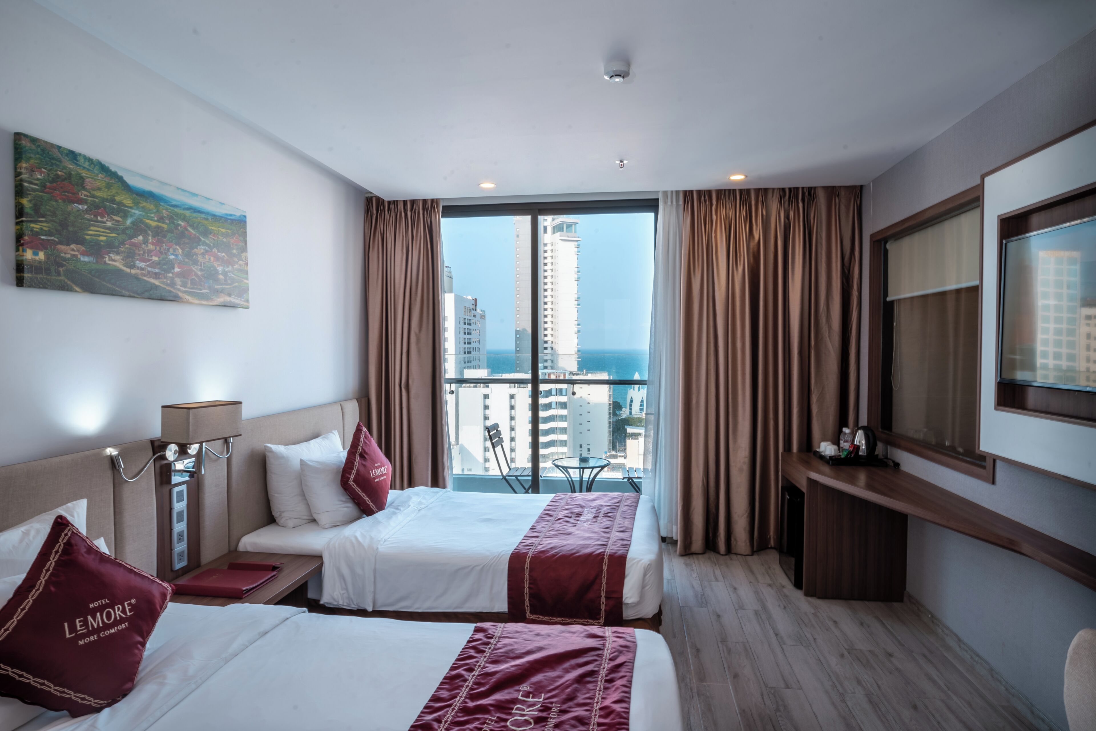 A hotel room with two beds, a painting, a view of the city, and a balcony with curtains.