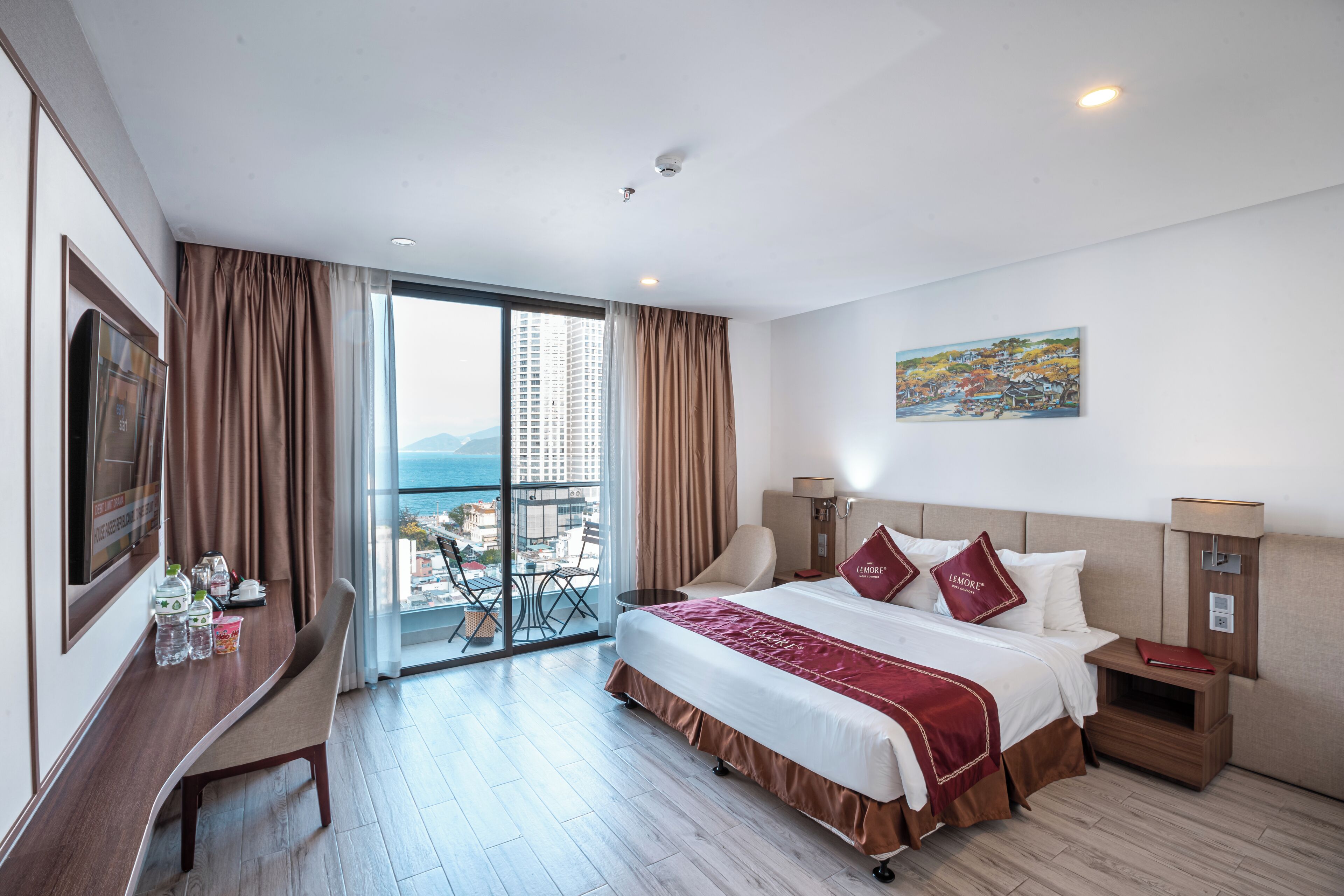 A hotel room with a large bed, a desk with a chair, a TV, and a view of the city and mountains through the window.