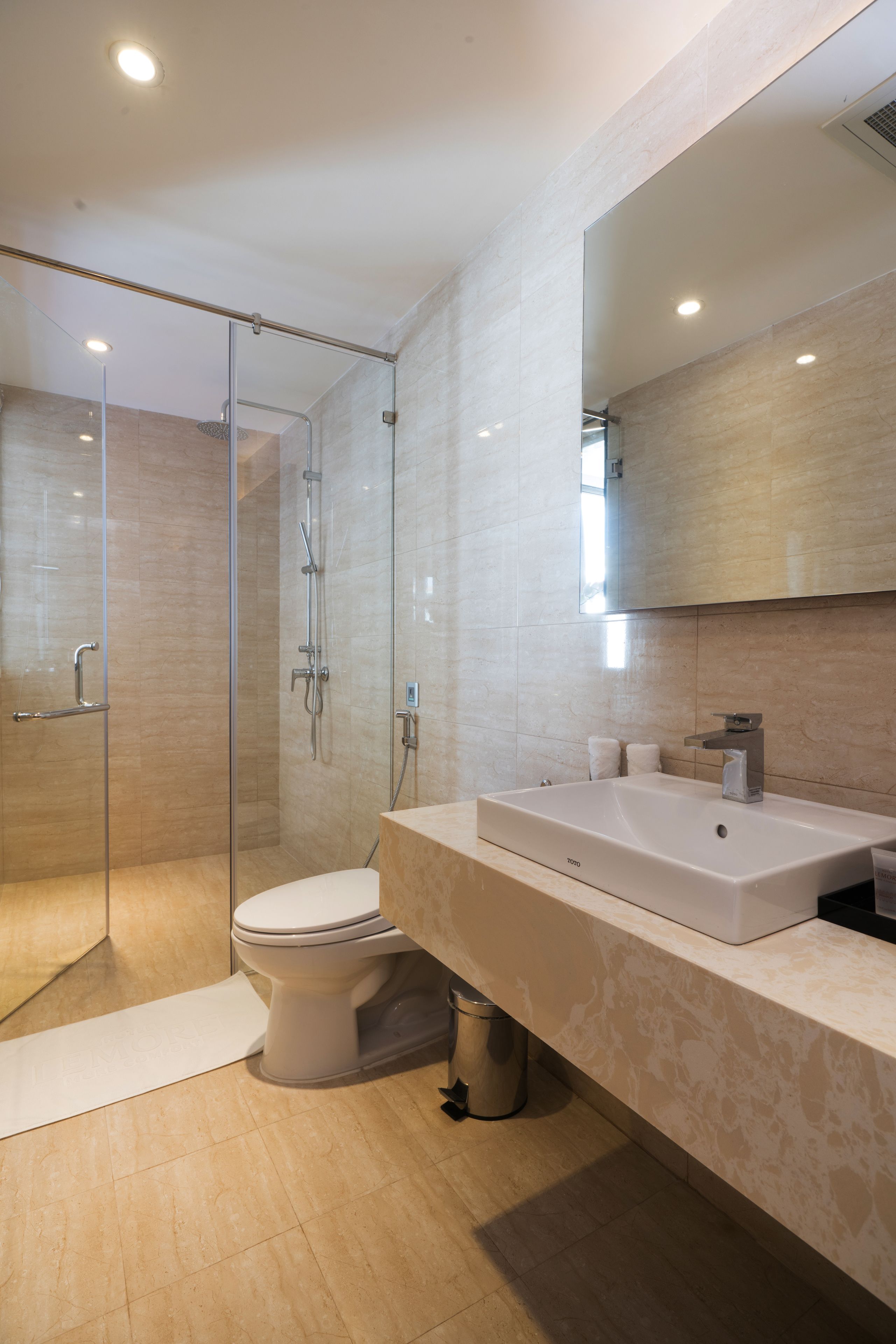 A modern bathroom with a glass-enclosed shower, a white toilet, and a large sink with a mirror above it.