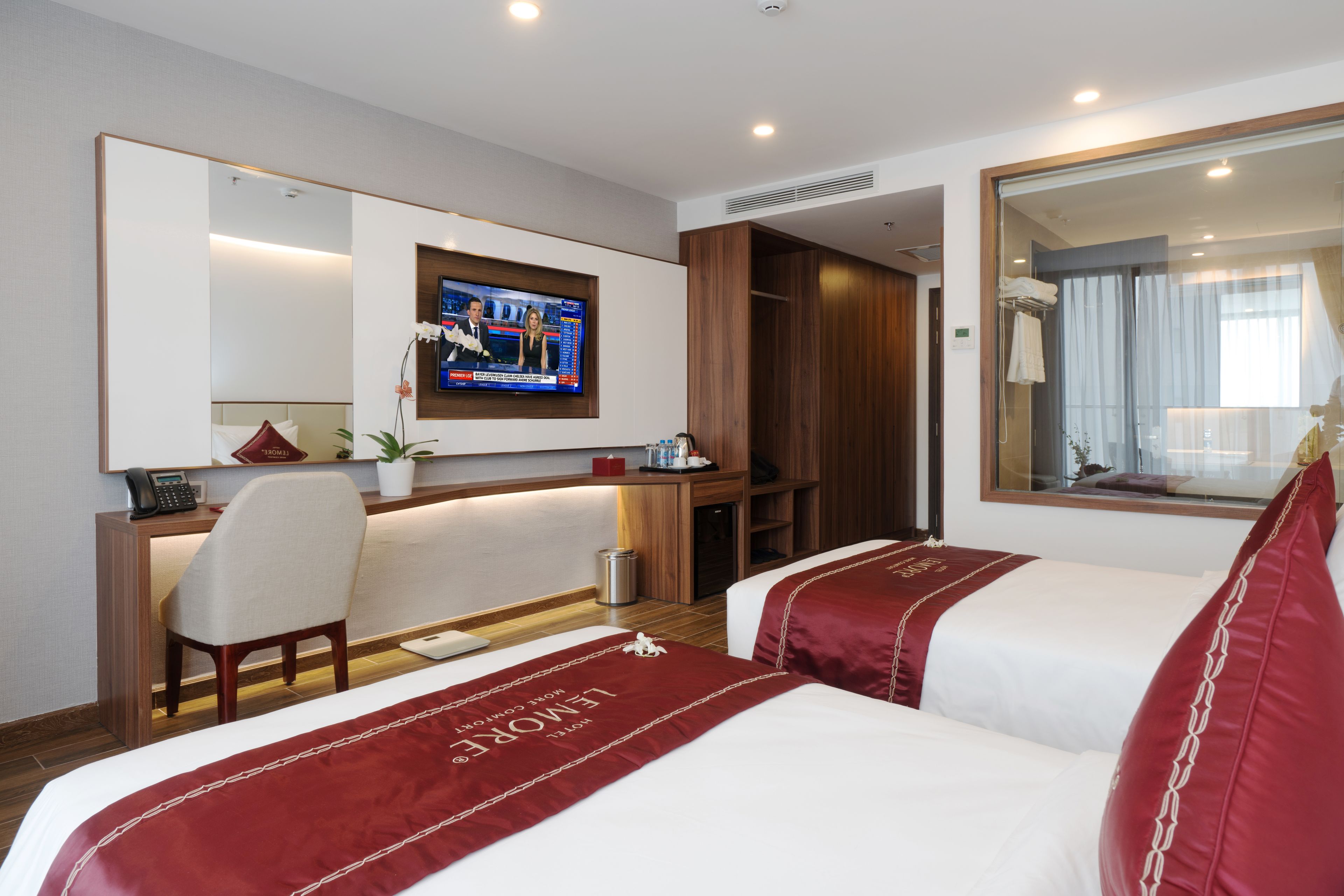 A hotel room with two beds, a desk, a television, and a large mirror.