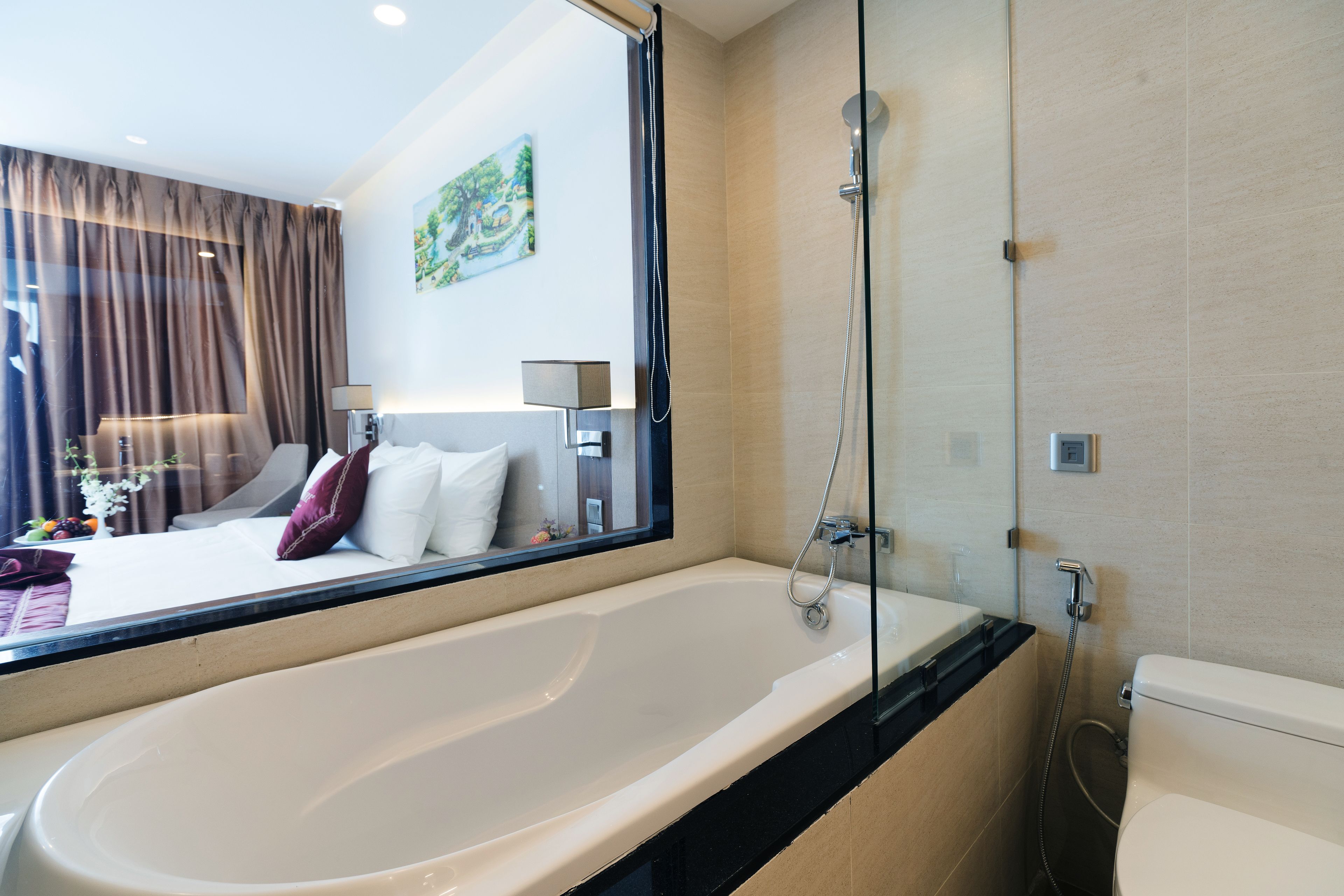 A modern bathroom with a large bathtub, a shower, and a toilet. There is a large mirror above the bathtub, and a painting on the wall.