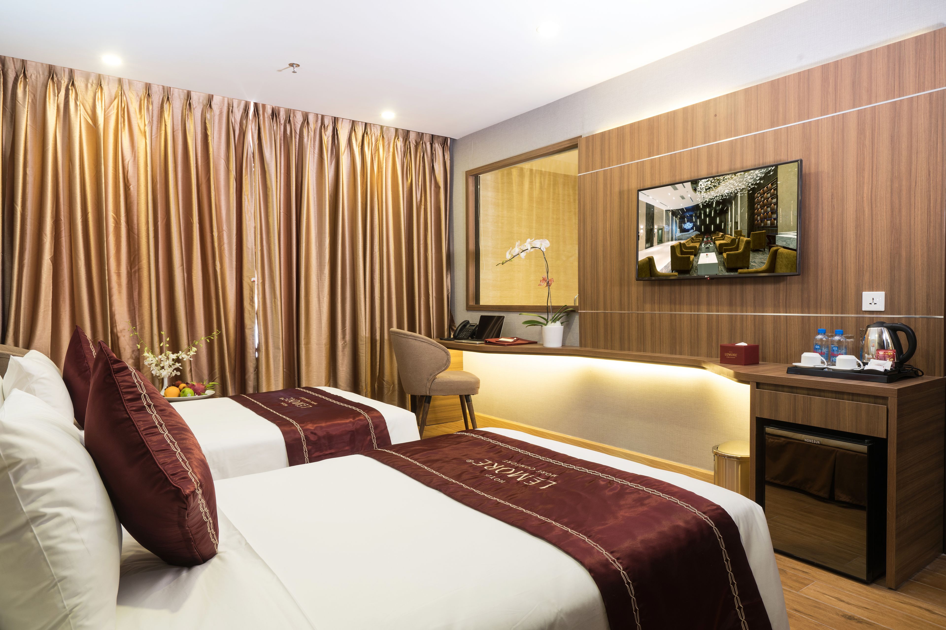 A hotel room with two beds, a desk, a chair, a minibar, and a large mirror.