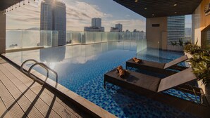 An infinity pool with lounge chairs and a glass railing overlooking a cityscape. - LeMore Hotel Nha Trang (Nha Trang)