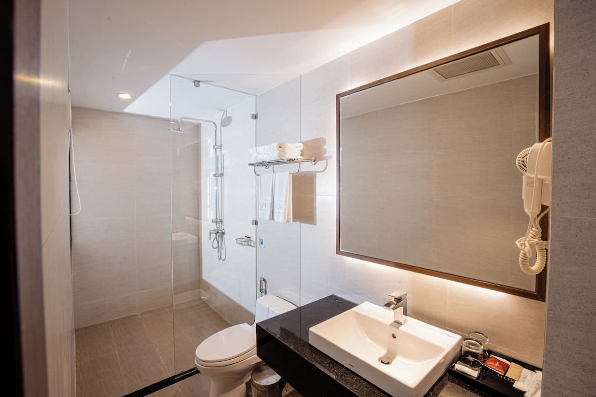 A modern bathroom with a glass shower enclosure, a white toilet, a black countertop sink, and a hairdryer mounted on the wall.