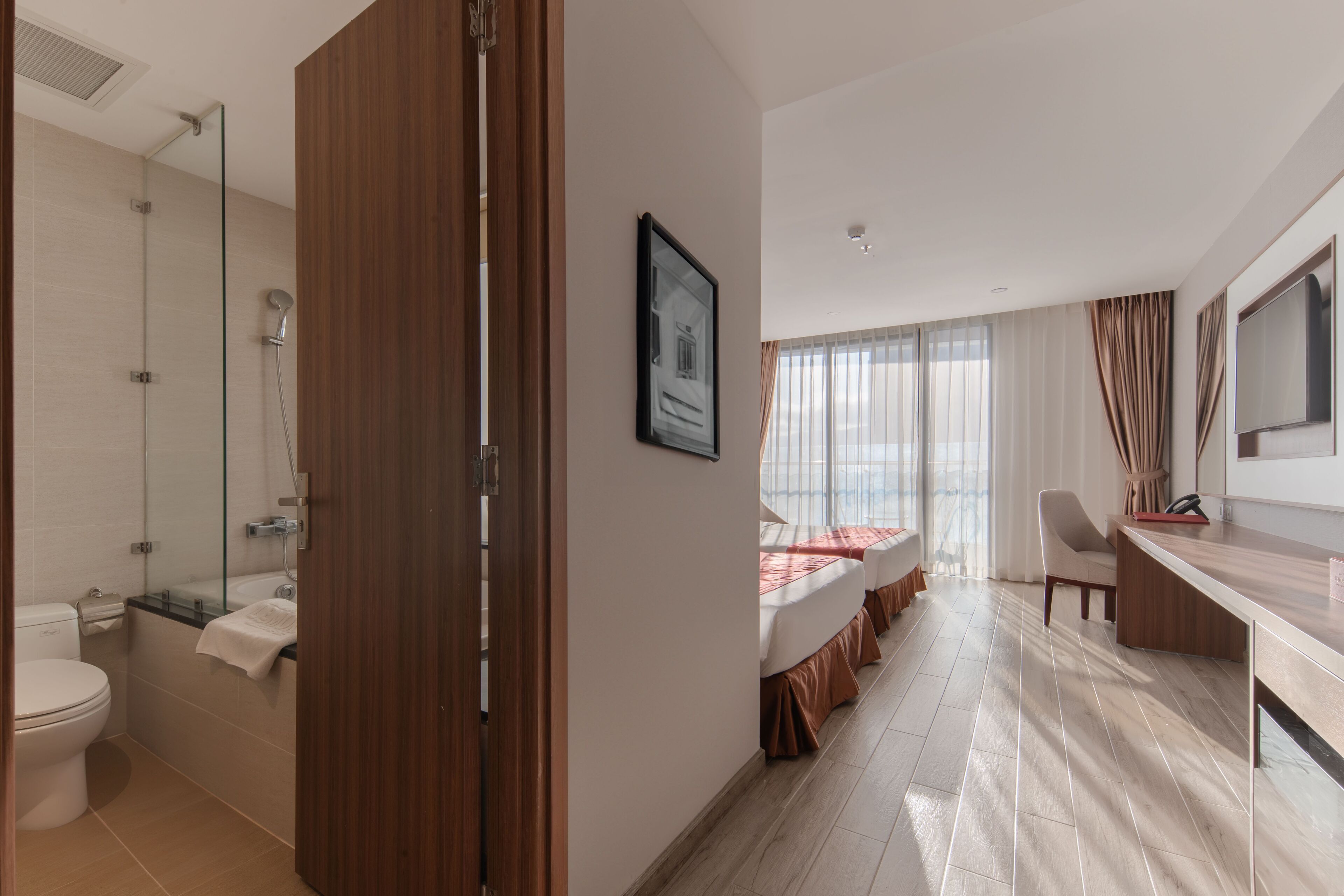 A modern hotel room with a shower, toilet, bed, desk, and a large window.