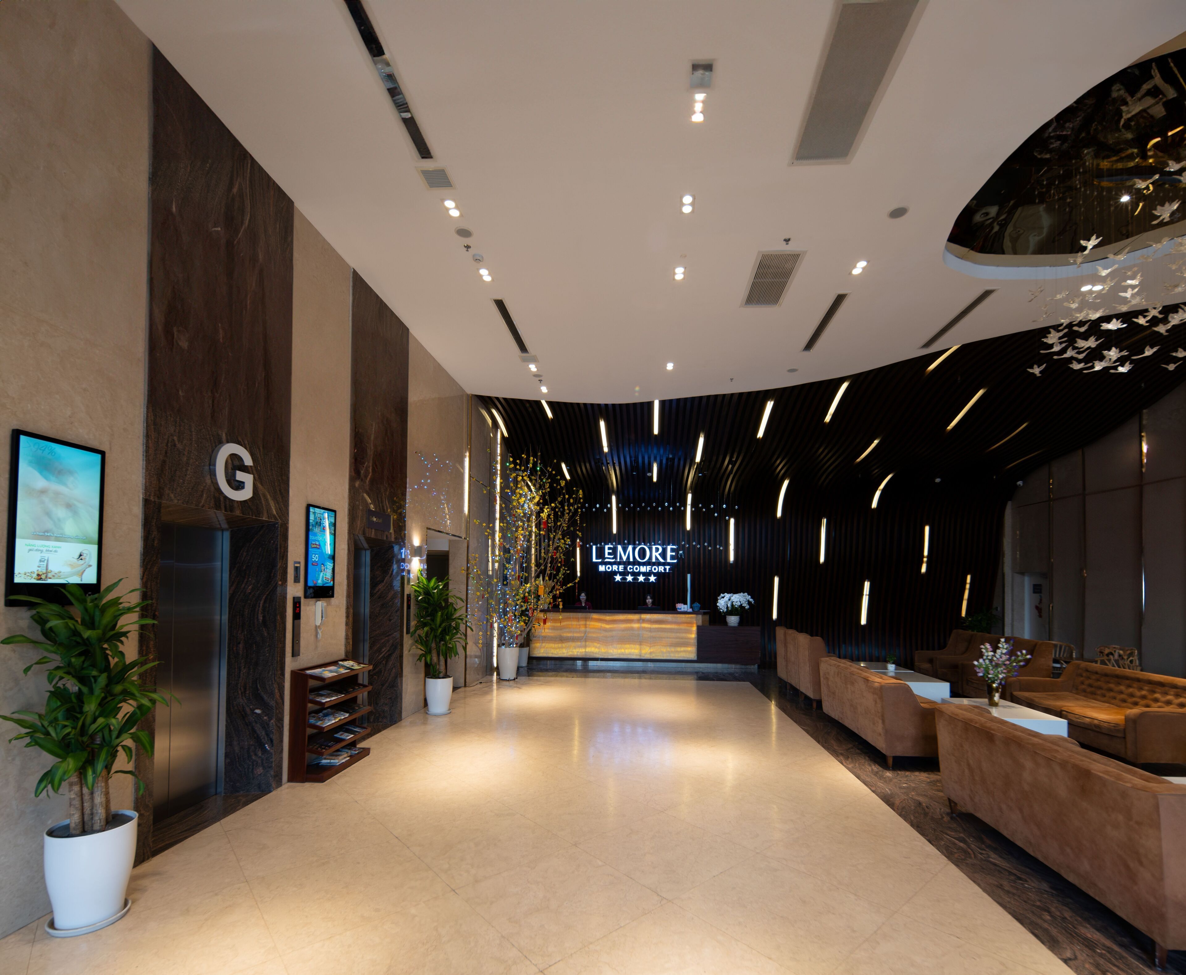 A modern hotel lobby with a reception desk, seating area, and a large potted plant.
