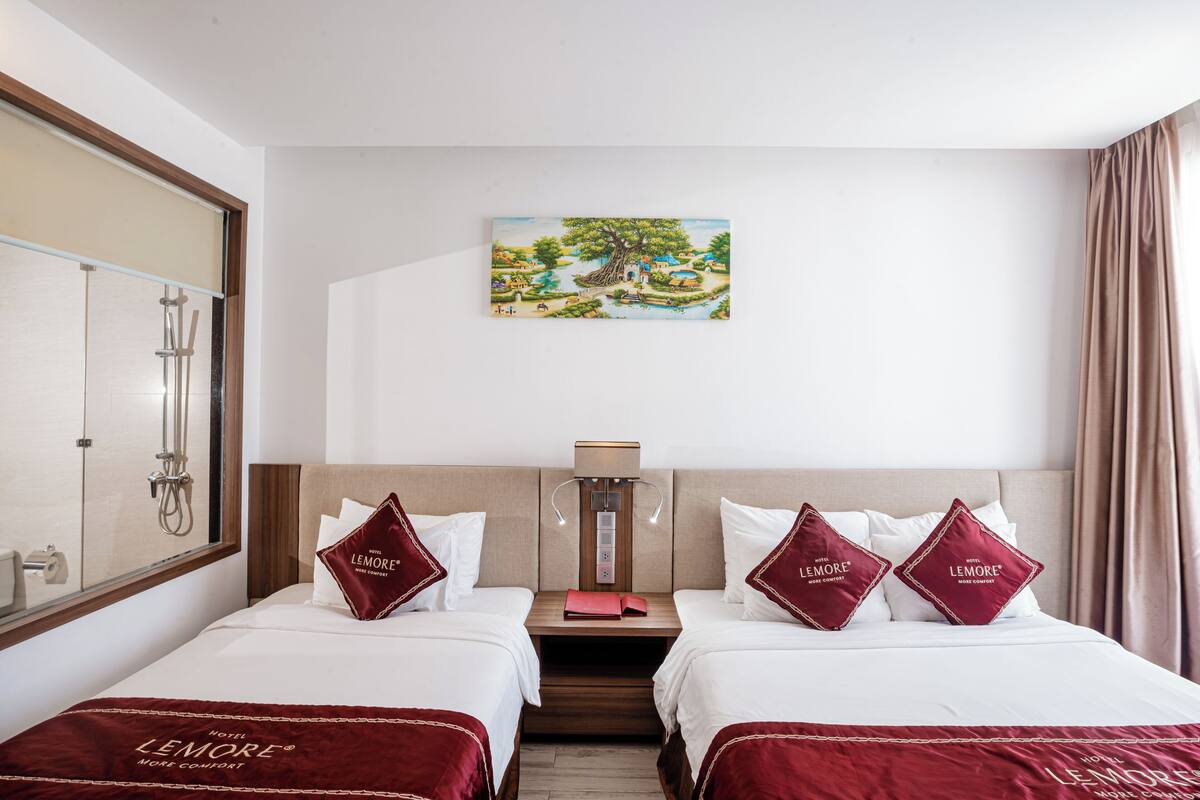 A hotel room with two beds, a painting of a landscape, a nightstand, and a lamp.