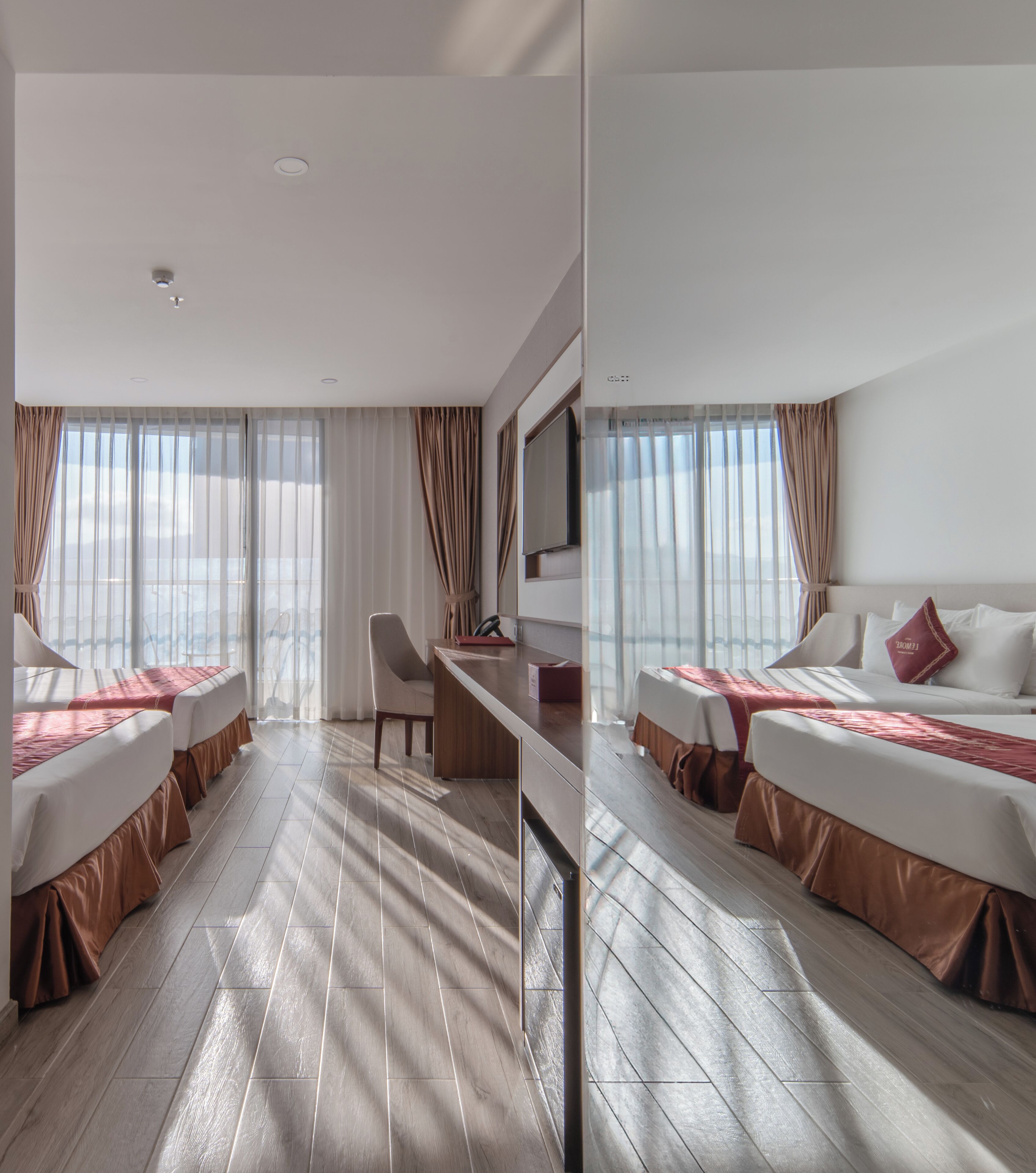 Habitación de hotel con dos camas, un escritorio, una silla y ventanas amplias con cortinas.