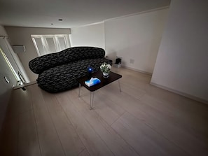 A modern living room with a black patterned sofa, a small coffee table with a book and a vase of flowers, and a door in the background.