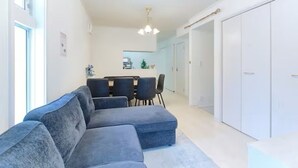 A modern living room with a sectional sofa, a dining area with a table and chairs, and a walk-in closet with hanging space. - Soshigaya Apartment (Tokyo)