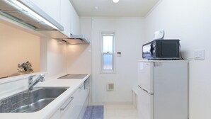 A compact kitchen with a sink, stove, microwave, and refrigerator. - Soshigaya Apartment (Tokyo)