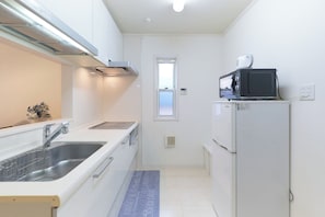 A compact kitchen with a sink, stove, microwave, and refrigerator. - Soshigaya Apartment (Tokyo)