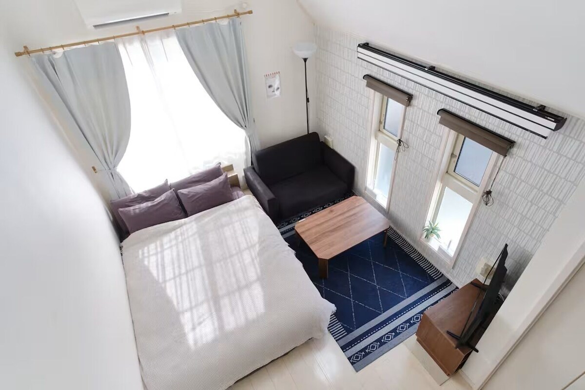 A compact room with a bed, a small sofa, a table, and a window.