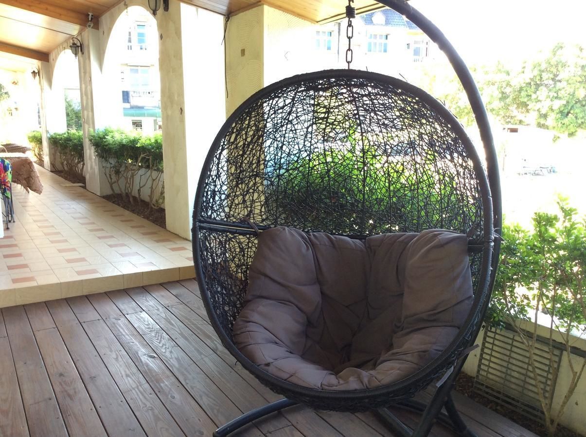 A hanging chair with a cushioned seat and back, suspended by a metal frame, on a wooden deck with a tiled floor.