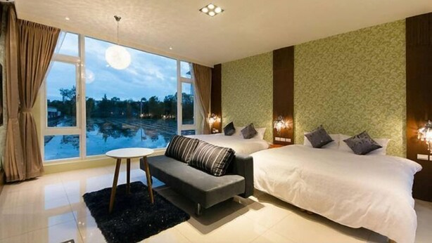 A modern bedroom with a large bed, a sofa, and a small table. There is a view of a swimming pool outside the window. - Tourist Home B&B (Luodong)