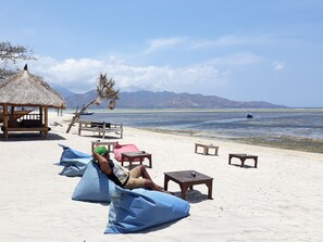 A beach with a thatched-roof hut, lounge chairs, and a wooden table.