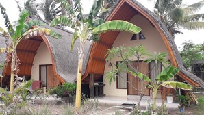 A bungalow-style building with thatched roofs and wooden beams, surrounded by tropical vegetation. - Ings Garden (Gili Air)