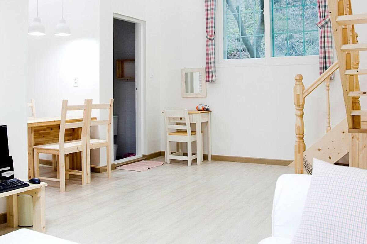 A spacious room with a wooden ceiling, a white sofa, a desk with a computer, a chair, and a staircase.