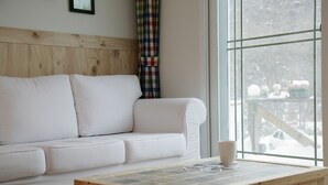 A white sofa, a wooden coffee table, and a window with a view of a snowy landscape. - Namubyeol (Gapyeong)