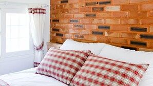 A bedroom with a brick-patterned headboard, a white bed with red and white checkered bedding, and a window with white curtains. - Namubyeol (Gapyeong)