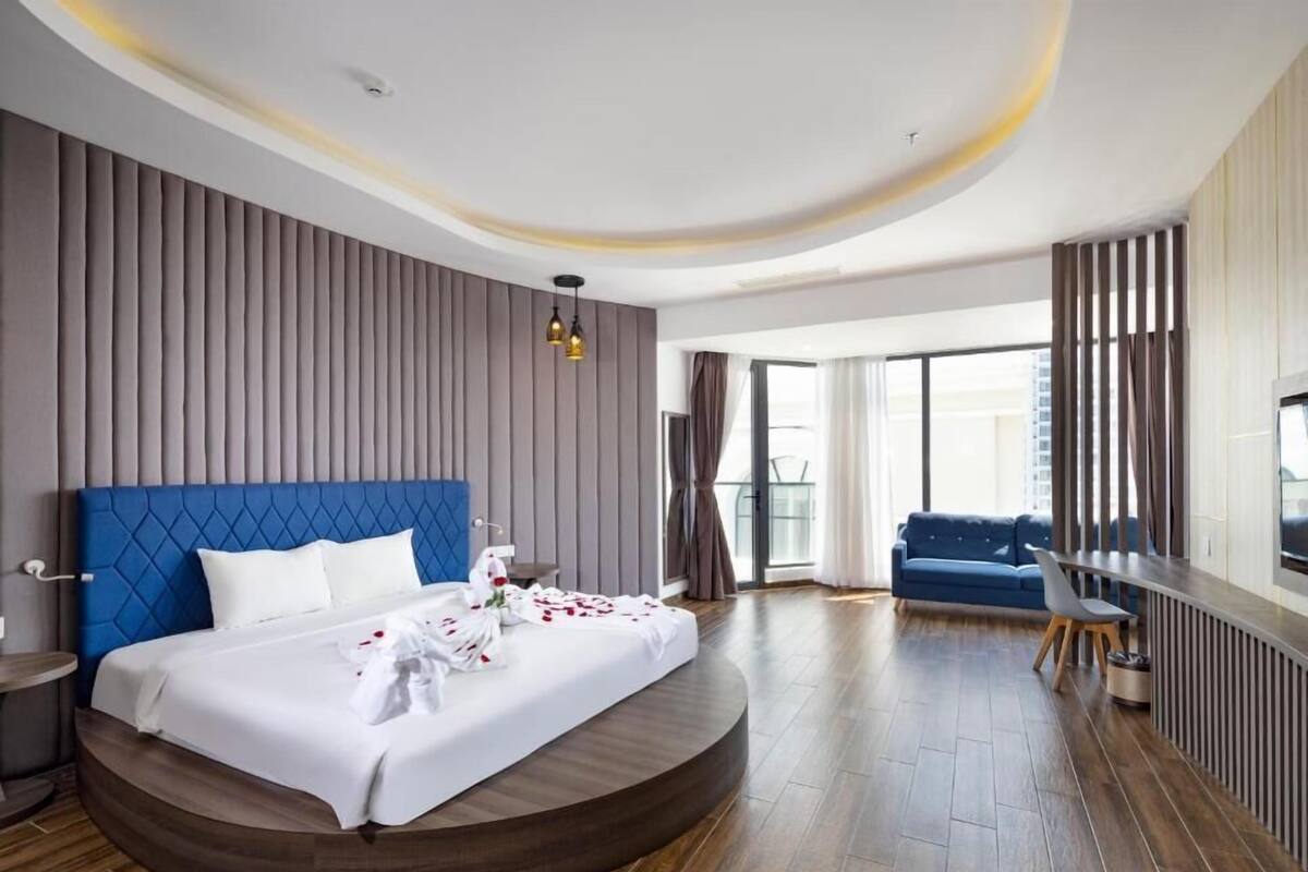 Une chambre d’hôtel moderne avec un lit aux lignes courbes, une tête de lit bleue et une grande fenêtre donnant sur la ville.