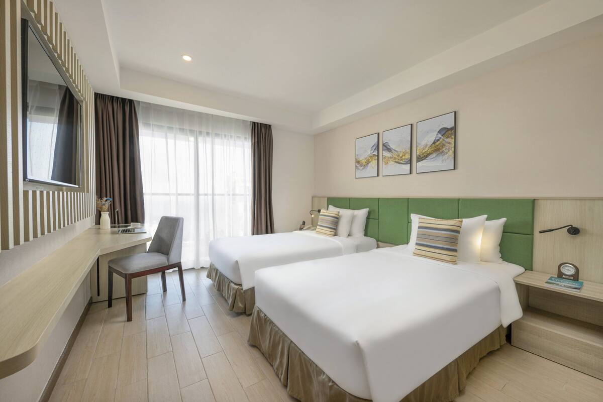 Une chambre d’hôtel avec deux lits, un bureau, une chaise et des œuvres d’art accrochées au mur.