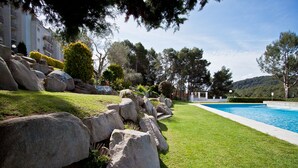 Una piscina rodeada de césped cuidado, rocas grandes y árboles.