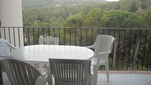Un balcón con una mesa redonda y cuatro sillas, con vista a una ladera boscosa.
