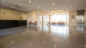 A spacious lobby with a reception desk, seating area, and a large window providing natural light. - Pacific Hotel Shiroishi (Shiroishi)