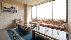 A modern hotel room with a large window, a traditional Japanese painting, a blue area rug, and a classic wooden coffee table. - Pacific Hotel Shiroishi (Shiroishi)