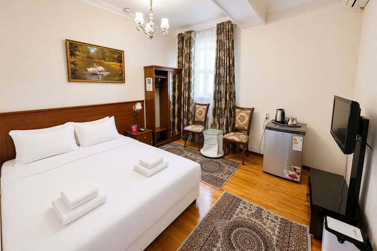 A hotel room with a bed, a desk with a television, a small refrigerator, and a painting on the wall.