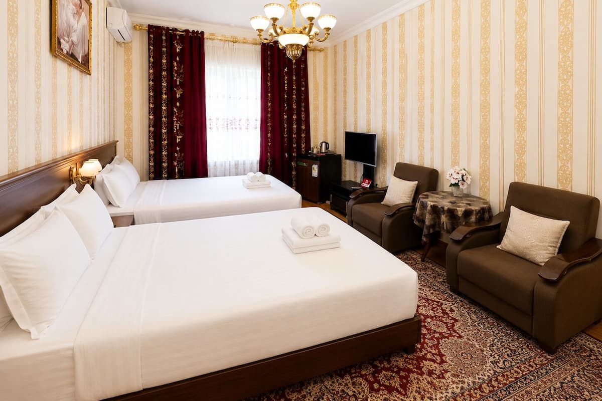 A hotel room with two beds, a sofa, a TV, and a small table with a vase.