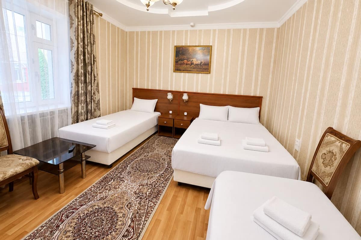A hotel room with two single beds, a double bed, a small table, a chair, a rug, and a painting on the wall.
