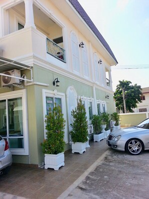 A two-story building with a balcony, potted plants, and a parked car. - PP Garden Villa (Phitsanulok)