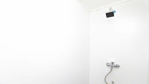 Een witte douchecabine met een handdouche en een bedieningspaneel aan de muur.
