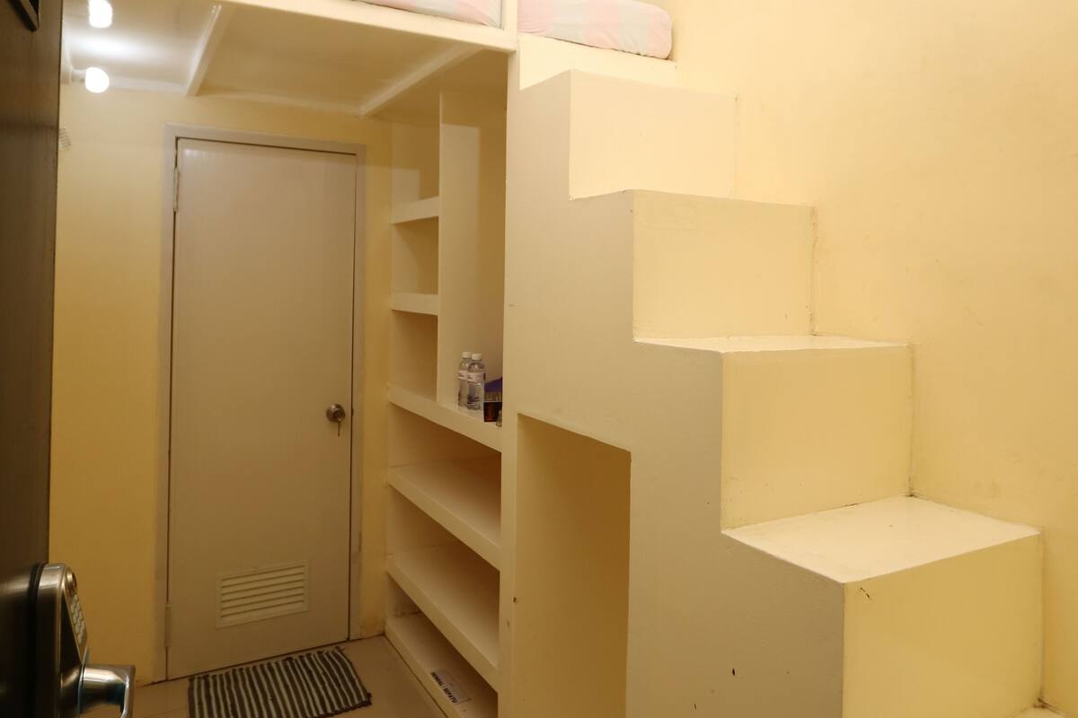 Een kleine kamer met een stapelbed, een deur en ingebouwde planken.