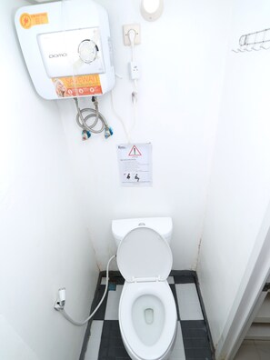Un baño pequeño y funcional con inodoro, calentador de agua y señal de advertencia.