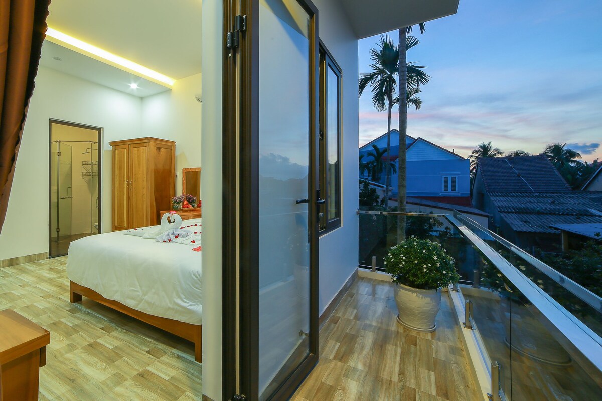 A bedroom with a bed, wooden wardrobe, and a balcony with a potted plant.