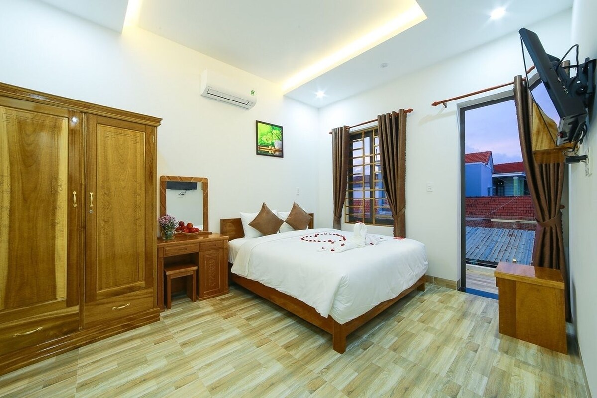 A bedroom with a bed, wooden wardrobe, desk, and a TV mounted on the wall.