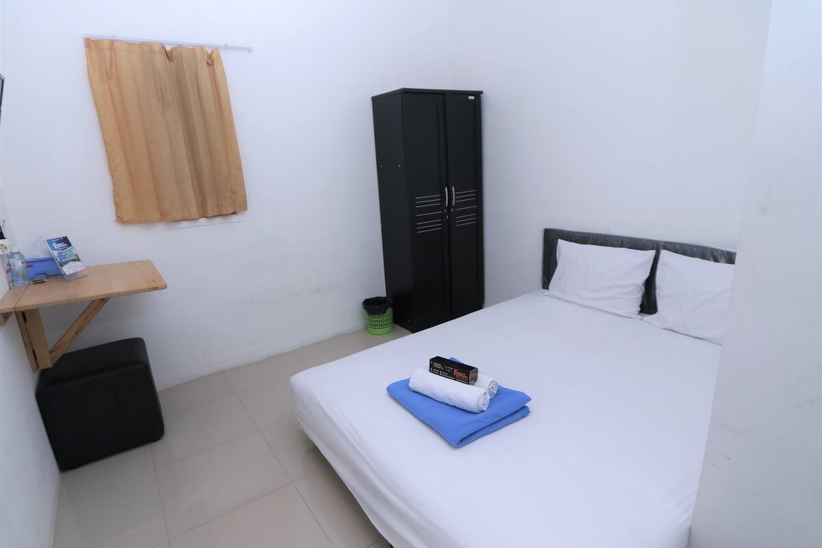 A hotel room with a bed, a desk, a wardrobe, and a curtain.