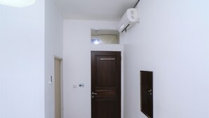 Een gang met een donker houten deur, een klein raam en een wandairconditioning.