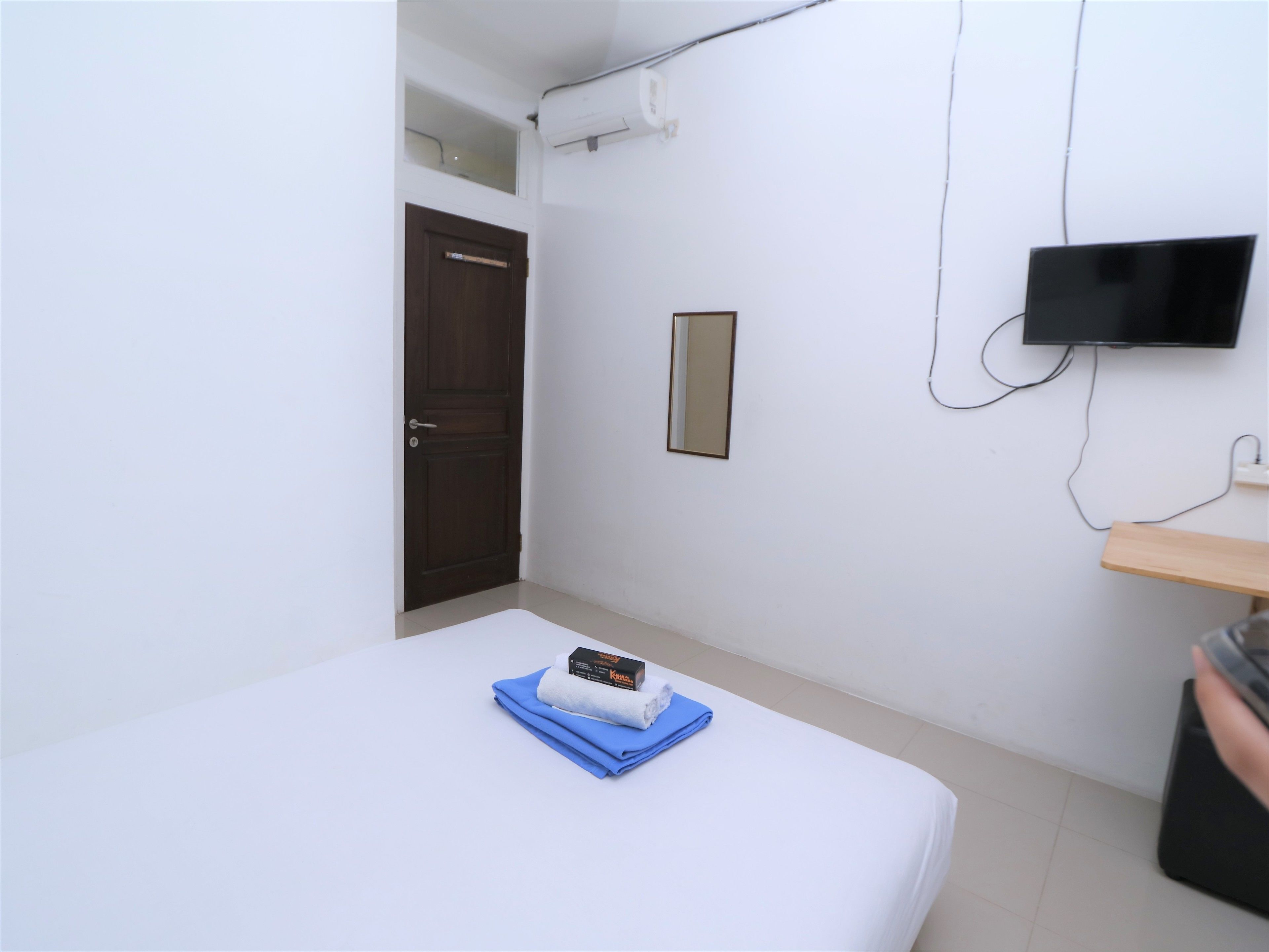 A hotel room with a bed, a TV mounted on the wall, a door, and a small table.