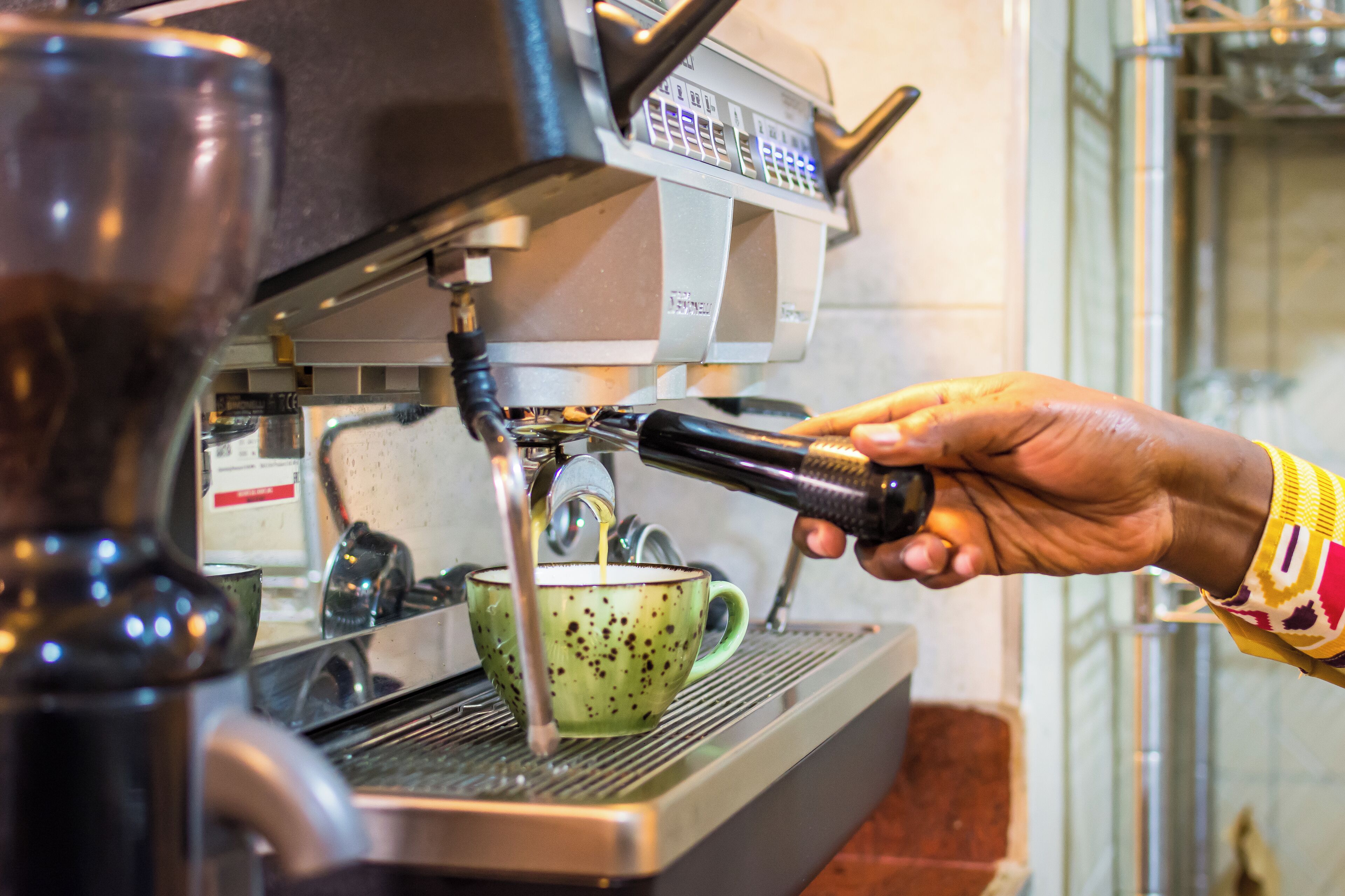 Una mano sosteniendo el portafiltro de una cafetera, con una taza verde debajo.