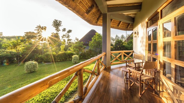 Une terrasse en bois dotée d’un toit de chaume, de rampes en bois et offrant une vue sur un jardin luxuriant et une montagne en arrière-plan.